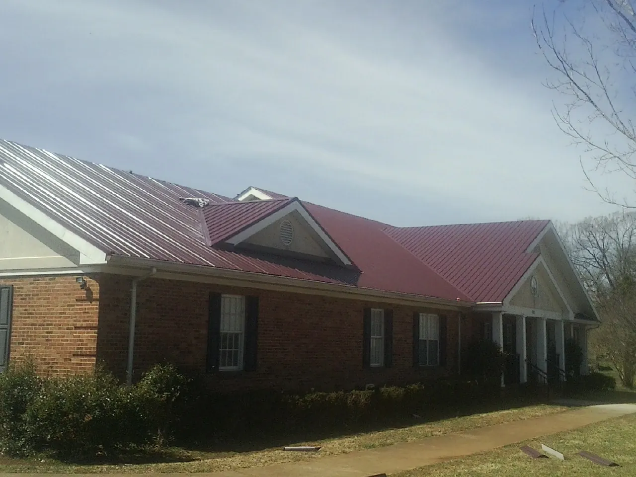 Red metal roof with gabled entries on a long brick building, from a Hail Damage Roof Repair job in Bethlehem